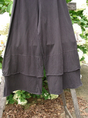 Bluefishfinder.com Barclay Cotton Lycra Crop 2 Petal Pantaloon in unpainted black, size 0, with layered petal-like hem panels and a soft cotton-lycra drape. The cropped garment hangs in front of leafy greenery, its dark matte fabric contrasting with the bright outdoor background.