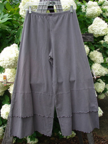 Bluefishfinder.com Barclay Cotton Lycra Crop 2 Petal Pantaloon in unpainted dusty plum, size 0, with a wide elastic waistband, soft drape, and scalloped petal hem. The cropped pantaloon hangs on a hanger against dense white hydrangeas and green foliage.
