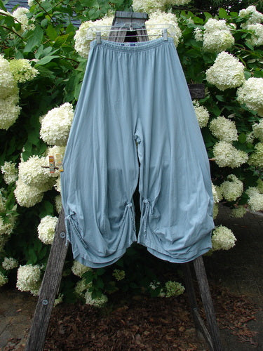 Bluefishfinder.com Barclay Crop Tie Bottom Crop 4 Square Pant in unpainted Blue Cloud, size 0, hangs in a soft drape with a wide gathered waistband, voluminous cropped legs, and tie details at the hem. The light blue fabric falls against a wooden ladder and white hydrangeas, with muted natural light emphasizing the smooth, airy texture.