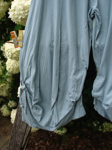 Bluefishfinder.com Barclay Crop Tie Bottom Crop 4 Square Pant in unpainted Blue Cloud, size 0, shown as loose blue cropped pants with gathered tie hems and a soft, draped fabric finish. The wide legs fall in relaxed folds beside white flowers and weathered wood.