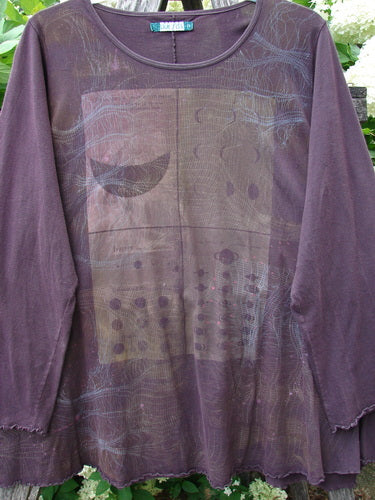 Bluefishfinder.com Barclay Long Sleeved Studio Cafe Tee in celestial purple plum, size 2, with a sheer long-sleeve silhouette, raw-edged hem, and a muted graphic print across the front. The lightweight fabric hangs softly against an outdoor leafy backdrop.