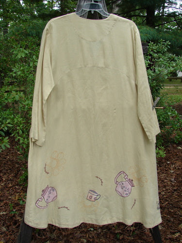 1999 Cream and Sugar Coat Pitcher Plantain OSFA: A long white dress with teapot and teacup patterns, featuring a wide lower drape, V-neckline, oversized shell button, and deep side pockets.