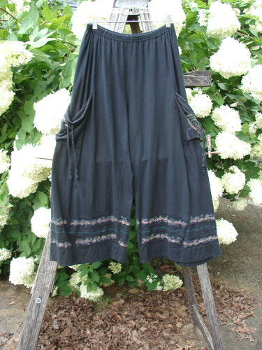 Bluefishfinder.com Barclay Crop Tie Pocket Pinch Pant Wind Chain Black Size 0, shown as loose black cropped pants with a gathered waist, side tie pockets, and a softly draped silhouette. Decorative chain-like trim bands the hem, while the lightweight fabric hangs against a leafy outdoor backdrop.