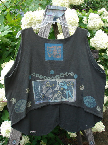 Bluefishfinder.com 1993 The Vest Dancer in black sand, a sleeveless vest with a soft drape and raw-edged armholes. It hangs on a wooden hanger, showing blue printed square motifs and circular accents across the front.