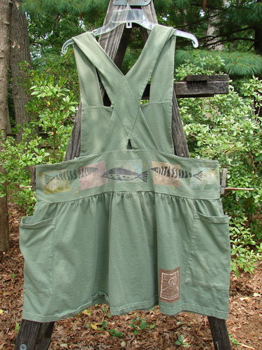 1995 Overall Jumper Fish Path Dinette Green OSFA displayed on a wooden pole, featuring a fish design, crisscross back straps, oversized side pockets, and a wide gathered skirt.