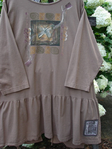 Bluefishfinder.com 1995 Clothespin Jacket Butterfly Mudpie OSFA in muted taupe, a long-sleeve tunic with a gathered ruffled hem and soft drape. The front shows a butterfly graphic framed by abstract blocks, with a small patch near the lower right hem.