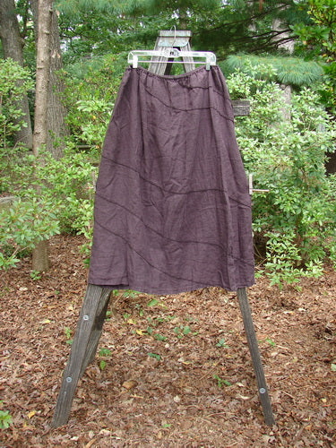 Barclay Linen Hemp Diagonal Skirt Unpainted Eggplant Size 2 displayed on a wooden clothes rack outdoors, showcasing its diagonal stitchery and woven texture.