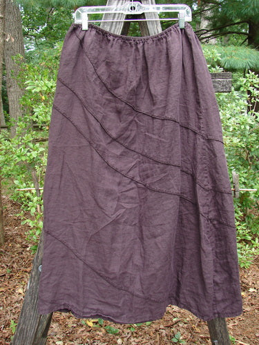 Barclay Linen Hemp Diagonal Skirt Unpainted Eggplant Size 2 displayed on a wooden pole outdoors, showcasing its diagonal stitchery and relaxed, flowing silhouette.