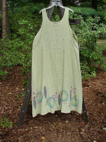 Barclay Linen Tank Dress Undersea Celery Size 2 displayed on a wooden ladder, featuring a floral pattern and a sweeping lower skirt. The dress has a rounded neckline and downward curved empire waist seam.