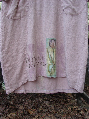 Bluefishfinder.com 1998 Botanicals Thostle Dress Single Tulip Mallow Size 1 in faded pink, a loose, linen-like dress with rounded patch pockets and a hand-painted tulip-and-mallow motif near the hem. The soft, wrinkled fabric hangs in a simple front view, with muted earthy tones and a worn matte finish.