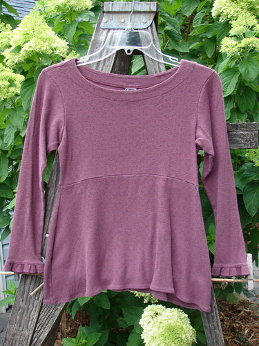 2000 Wool Pointelle Anais Top Unpainted Murple Tiny Size 0 displayed on a wooden fence, highlighting its intricate lettuce edging, empire waist seam, and fitted, breathable merino wool fabric.