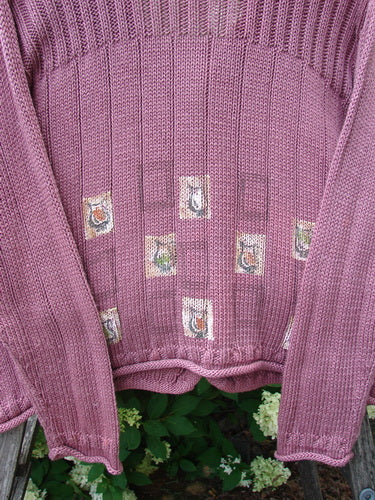 Bluefishfinder.com 1999 Triangle Cardigan Sweater in pitcher clay, size 1, with a ribbed knit texture and long sleeves. The mauve-pink cardigan shows small square patch motifs across the front, with a softly draped hem against leafy greenery.