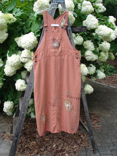 Bluefishfinder.com 1998 Botanicals Planters Overall Jumper Leaf Mimosa Size 0 in faded rose pink, a sleeveless overall-style dress with wide shoulder straps, front bib, and leaf-and-mimosa botanical print. It hangs from a wooden ladder outdoors, framed by dense white hydrangea blooms and dark green foliage.