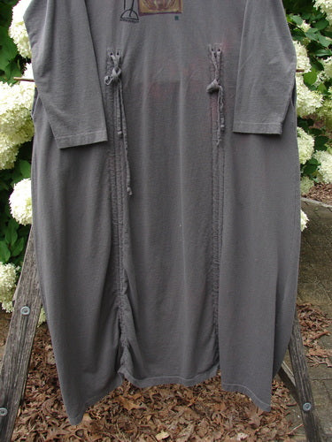 Bluefishfinder.com 1998 Cornucopia Dress Fall Garden Eggplant Size 1 in muted eggplant gray, a loose long-sleeve dress with a soft drape, front tie details, and an asymmetrical hem. The garment hangs outdoors against greenery and wood, with diffuse natural light emphasizing its matte knit texture.
