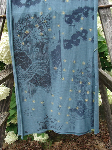 Bluefishfinder.com Barclay Diagional Scarf Wrap Stary Night Garden Blue Hunter OSFA, a sheer blue wrap with a diagonal drape and scattered gold star motifs. Its soft, lightweight fabric shows layered navy floral and landscape-like patterns, hanging against rustic wood and greenery.