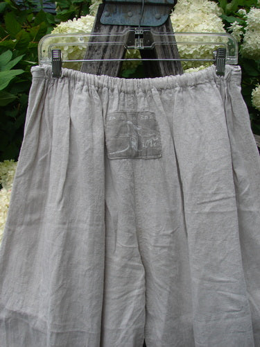 Magnolia Pearl Homespun Linen Ruffle Eyelet Bloomer in natural OSFA, shown as loose, gathered linen bloomers with a soft crinkled texture, elastic waistband, and a small centered patch. The pale neutral fabric hangs from a hanger against leafy greenery.