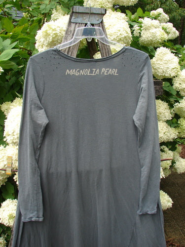 Bluefishfinder.com Magnolia Pearl Cotton Jersey Dylan Dress Fairy Ozzy OSFA in gray cotton jersey, with a loose long-sleeve silhouette and raw-edged seams. The back neckline is printed with Magnolia Pearl, and the dress hangs on a clear hanger before pale hydrangea blooms.