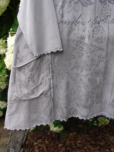 Barclay Cotton Lycra 2 Pocket Urchin Dress Flower Tops Size 0 in soft gray, with a floral print, scalloped hem, and two visible pockets. The lightweight cotton-lycra fabric drapes in layered panels, photographed close against greenery and weathered wood.