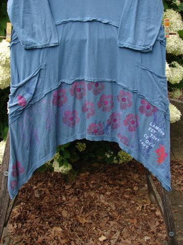 Bluefishfinder.com Barclay Raw Seam Vector Tunic Dress in Echo Blue, size 1, shown as a loose blue tunic with raw seam edges, long sleeves, and layered panels. The lower hem carries daisy and floral graphics in pink and purple over soft textured fabric.
