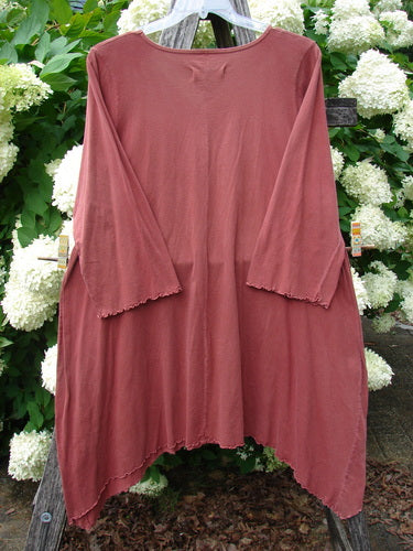 Bluefishfinder.com Barclay Three Quarter Sleeve Color Wheel Tunic in Tulip Dream Clay, size 1, shown as a dusty rose tunic with a soft drape, wide three-quarter sleeves, and a gently flared hem. The lightweight fabric hangs against a leafy floral backdrop.
