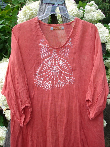 Bluefishfinder.com Barclay Linen High Vent Venetian Dress Center Starburst Poppy Size 1, a poppy-red linen dress with a loose V-neck silhouette, three-quarter sleeves, and a white starburst print centered on the chest. The airy, softly crinkled fabric hangs from a clear hanger against leafy white hydrangeas.