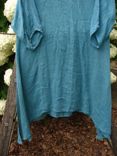 Bluefishfinder.com Barclay Linen High Vent Venetian Dress in unpainted jade, Size 1, shown as a loose linen garment with a softly wrinkled texture, wide sleeves, and a high-vent hem that hangs unevenly in teal-blue light.