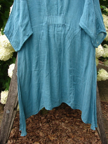 Bluefishfinder.com Barclay Linen High Vent Venetian Dress, unpainted jade, in size 1. The loose linen dress drapes in a soft A-line silhouette with short sleeves, a high vent hem, and a gently wrinkled texture, outlined against a rustic outdoor display.