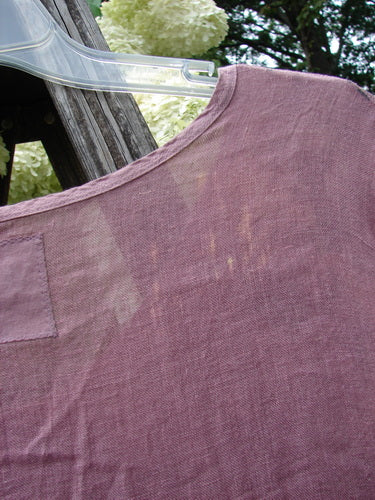 Bluefishfinder.com Barclay Linen Wave Pocket Dress, size 1, in dried sprig tulsi rose linen. The close-up shows a softly textured mauve-purple shoulder and upper bodice on a clear hanger, with visible weave, gentle wrinkles, and a small pocket flap near the edge.