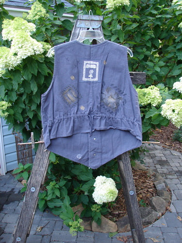 1995 Denim Invention Vest Fern Flower Madderlake Altered OSFA displayed on a wooden rack, showcasing superior lightweight fabric, metal buttons, varying hemline, V-neckline, draw cord back, and blue fish patch.