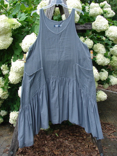 Bluefishfinder.com Barclay Gauze Batiste Summer Frock Jumper in unpainted gray day stripe, a sleeveless gauzy dress with a V-neck, ribbed bodice, gathered waist, and draped skirt. It hangs outdoors on a wooden stand amid white hydrangeas and green foliage.