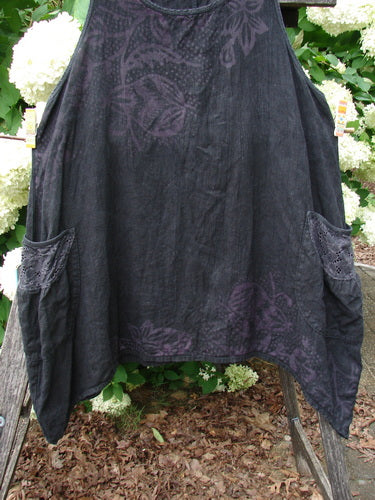 Bluefishfinder.com Barclay Summercloth Lace Two Pocket Pinafore in Moody Night Bloom black, a sleeveless dress with a soft lace-like texture and two large front pockets. The dark fabric shows subtle purple floral patterning and a loose, draped silhouette.