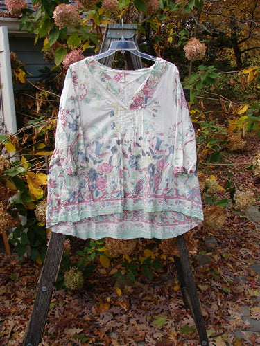 Magnolia Pearl European Cotton Breeze Blouse Spring Florals OSFA, featuring a lightweight floral pattern with raw edges, vertical pleats, and button cuff accents, displayed on a plastic swinger.