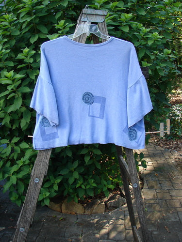 1997 Cotton Cashmere Short Sleeved Crop Pullover Geometric Skylark OSFA, featuring wide draped sleeves and geometric print, hangs on a weathered wooden ladder against leafy shrubs, embodying Bluefishfinder.com's unique vintage style.