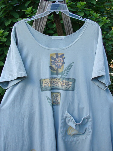 1995 Hop Scotch Dress Garden Friends Beach Glass Size 2, featuring a loose A-line shape, scooped neckline, decorative cross-shaped graphic, and elastic-topped pocket, hanging against a backdrop of green shrubs.