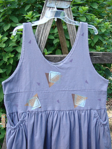 1996 Amusement Jumper Triangle Shadow Mulberry Size 1: A sleeveless, muted purple-gray sundress with geometric prints, featuring a scoop neckline, gathered skirt, elastic side pockets, and a drawcord back.