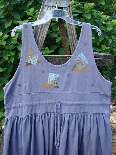 1996 Amusement Jumper Triangle Shadow Mulberry Size 1 features a sleeveless, scoop-neck design with a geometric print bodice, drawstring waist, and loose skirt, hanging on a ladder amidst greenery.
