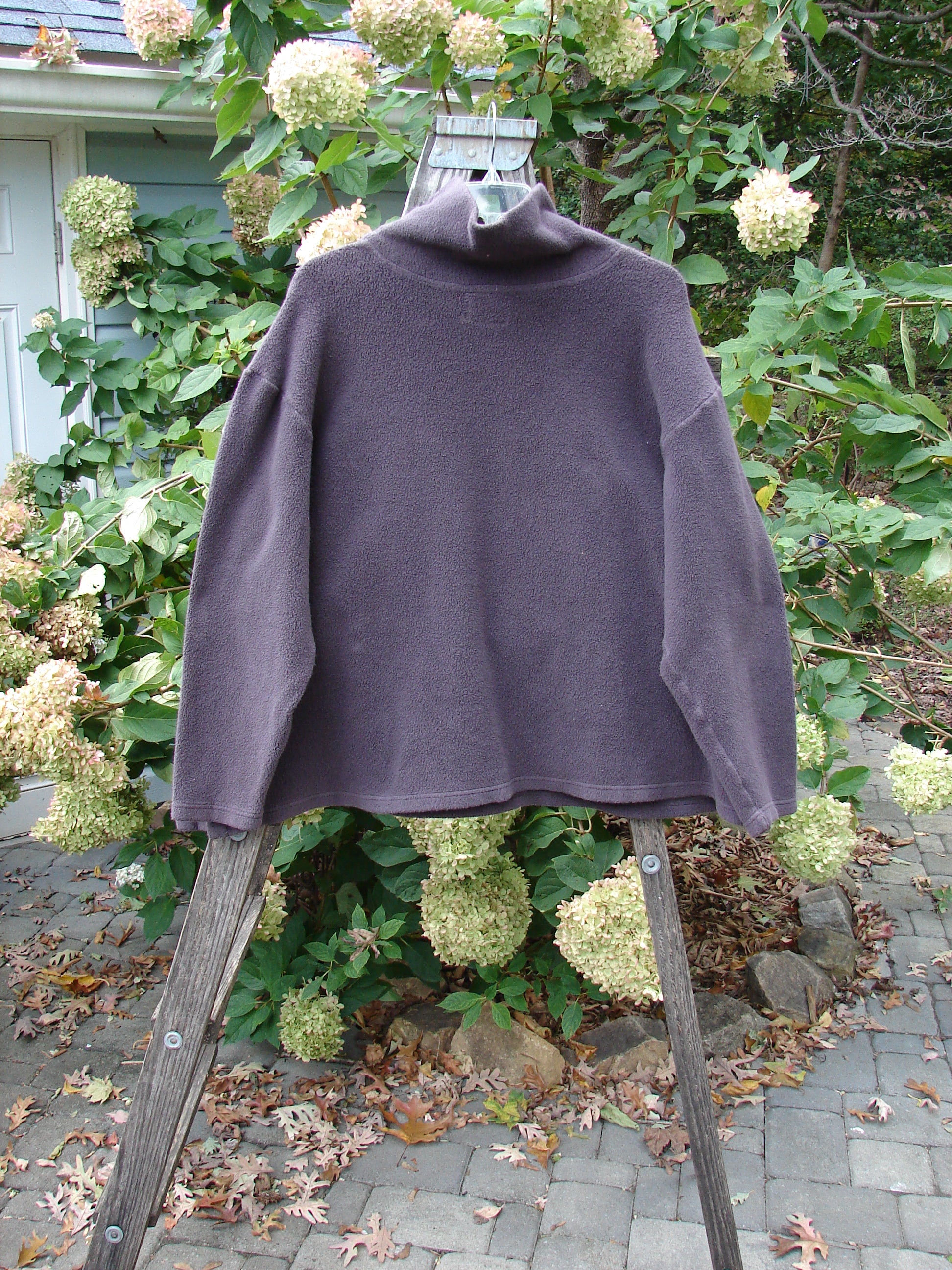 Barclay Patched Celtic Moss Big Collar Top Silly Pup Aubergine Size 1 displayed draped over a wooden ladder, showcasing its oversized A-line shape and unique plush texture.