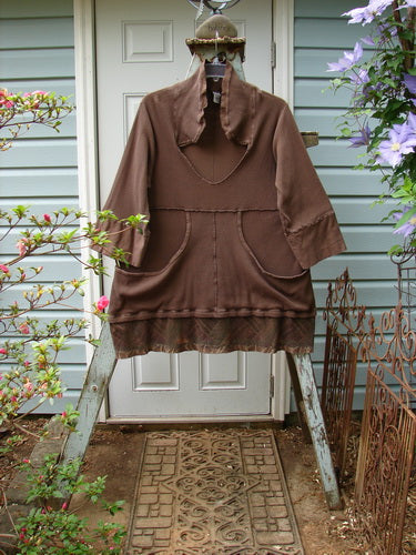 A Barclay Thermal Flutter Neck Kangaroo Pocket Top in Mud, featuring a longer flop sailor-like collar, a deep V-shaped neckline, and dual cargo drop front pockets. The top has banded lower sleeves, curly exterior stitchery, and sectional panels. The painted flutter hemline is done in the leaf theme paint, creating a generous square boxy shape. Bust: 52, Waist: 52, Hips: 56, Sweep: 60, Length: 35 inches.