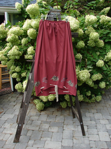 1992 Buttonloop Skirt Pomegranate Music OSFA: A cotton skirt with a drawcord waist, bell shape, and varying hemline, adorned with buttonholes and hand-dyed silk ribbon.