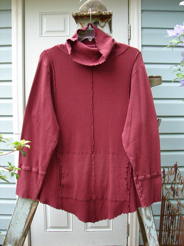 A burgundy Barclay Thermal Reverse Stitch Tunnel Pocket Top, size 2, with a floppy turtleneck and a kangaroo tunnel pocket. Features vertical sectional seams and a unique cut for a beautiful drape and sway.