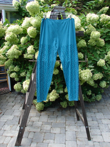 A Barclay Cotton Lycra Bally Layering Pant Legging in Aqua, size 2. A pair of blue pants on a clothes rack, featuring a continuous criss-cross theme paint. Perfect condition, made from medium weight cotton lycra. Full elastic waistband, longer slightly narrowing lower, and average length legging. A fun layering piece with a soft forgiving feel. Interior signature Blue Fish patch. Waist relaxed 28, waist fully extended 40, hips 42, inseam 29, length 40 inches.