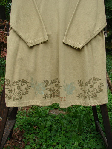 1998 Botanicals Bell Flower Top Plante Stem Size 1: A long-sleeved beige shirt on a swinger, featuring a wood post and a green plant.