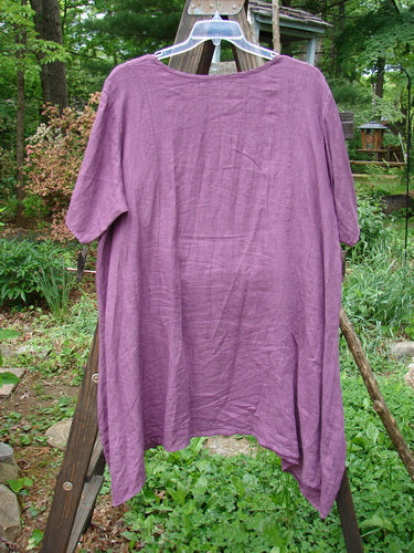 Barclay Linen Figure 8 Tunic Dress Garden Shadow Red Plum Size 2: A purple shirt on a clothes rack, showcasing the unique design with sectional curved figure eight front and rear seams, a full sweeping lower, and a varying hemline.