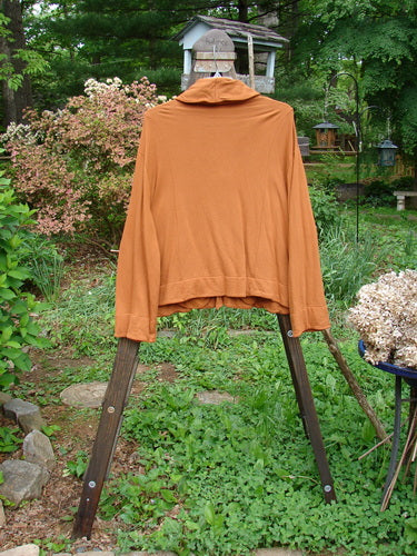 Image: A jacket on a rack with a long-sleeved shirt, a brown jacket, and a teddy bear nearby. 

Alt text: Barclay Fleece Two Button Jacket Vinery Gourd Size 1 on a clothes rack with other clothing items and a teddy bear.