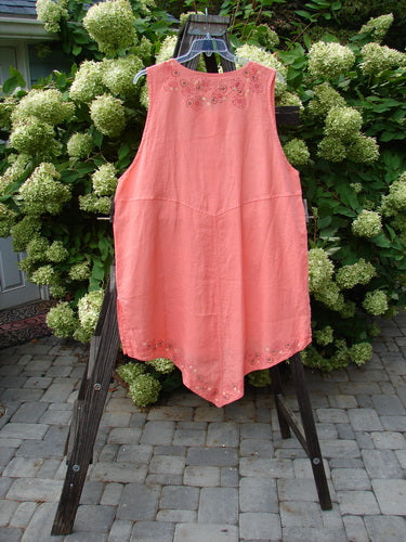 A medium weight linen Barclay Linen Katy Vest in Tangerine, size 2, displayed on a clothes rack. Features include thick pearly buttons, a varying hemline, oval neckline, painted drop pockets, and deeper arm openings.