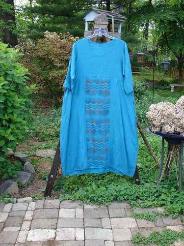 Barclay Linen Long Urchin Dress Center Wave Aqua Size 1: A blue dress with a pattern on it, featuring a rounded neckline, three-quarter sleeves, and deep side pockets.