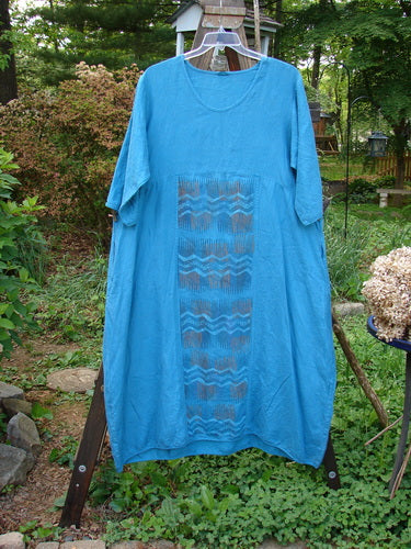Barclay Linen Long Urchin Dress Center Wave Aqua Size 1: A dress on a rack with a pattern, rounded neckline, empire waist, and three-quarter sleeves.