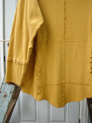 Barclay Thermal Reverse Stitch Tunnel Pocket Top Unpainted Mustard Size 1: A yellow sweater on a ladder, with a curly cowl neck and kangaroo tunnel pocket.