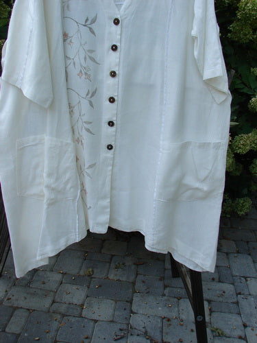A white linen jacket with double tie back and floral side sprig design. Features a deep V-shaped neckline, A-line sweep, and front drop flop pockets. Size 2.
