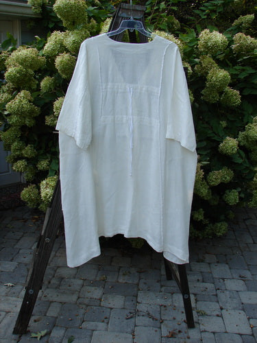 A white linen jacket with double tie back and floral side sprig design. Features a deep V-shaped neckline, A-line sweep, front drop flop pockets, and varying hemline. Size 2.